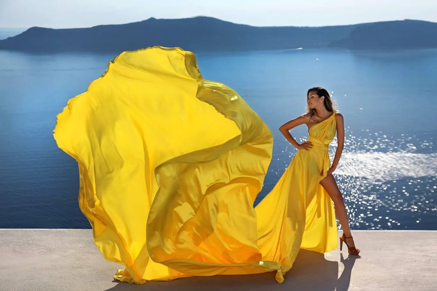 Yellow flowing-dress fashion image against sea and white architecture.